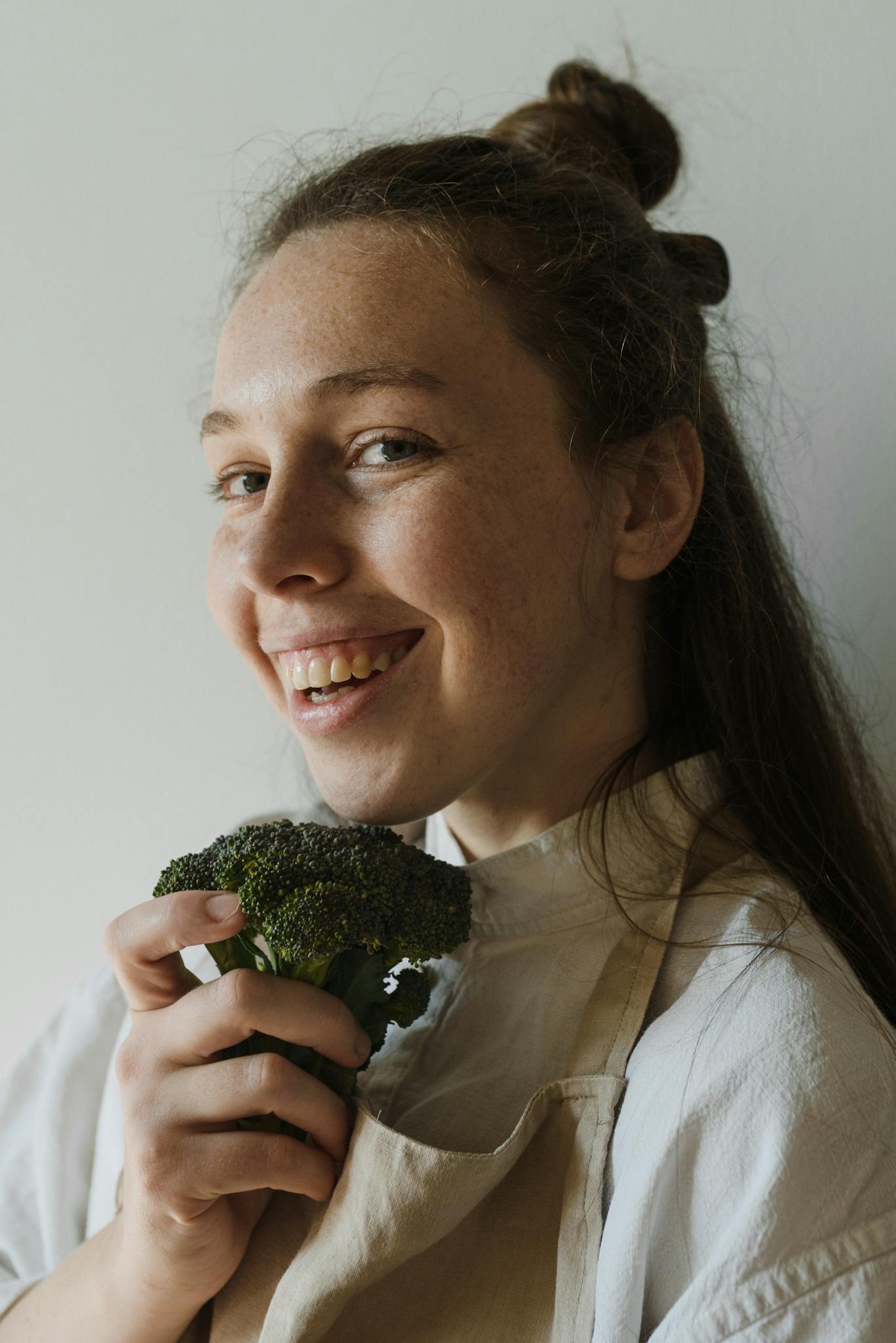 A woman with a joyful expression holds fresh broccoli, embracing healthy living.